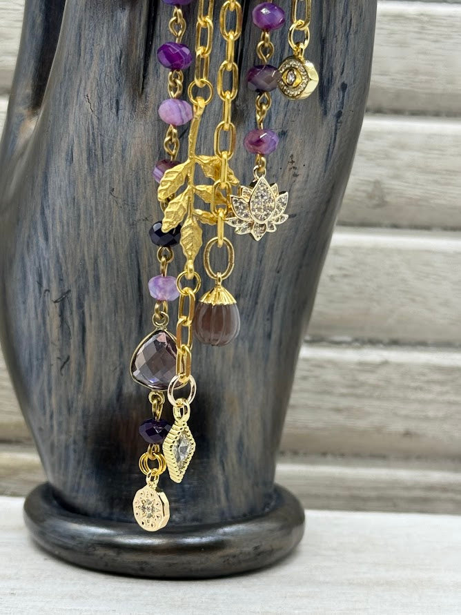 A closeup of the charms on the ear hanger showing a lotus charm, two cz charms, and two purple colored charms.