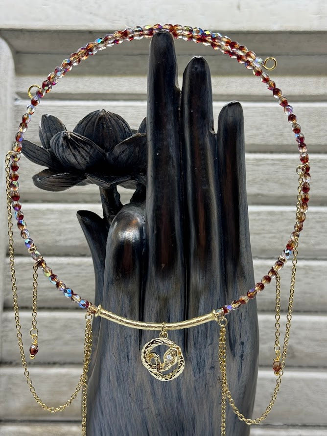 A statue of a hand is holding up a choker with red beads. There is a snake charm and gold chains hanging off the choker.