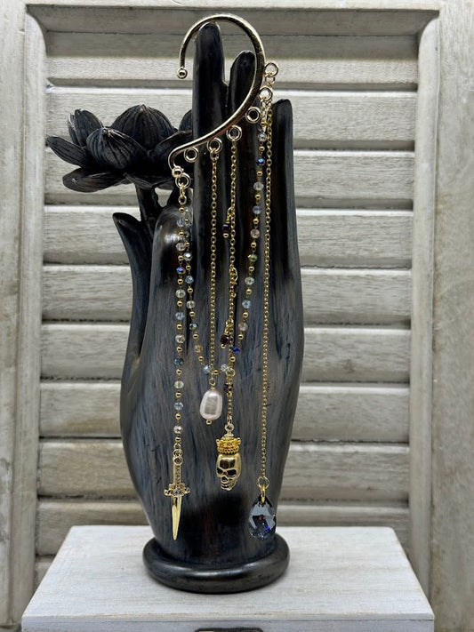 an ear hanger with beaded and gold chains with a cz dagger charm, a skull charm, a pearl, and a black rhinestone bead.