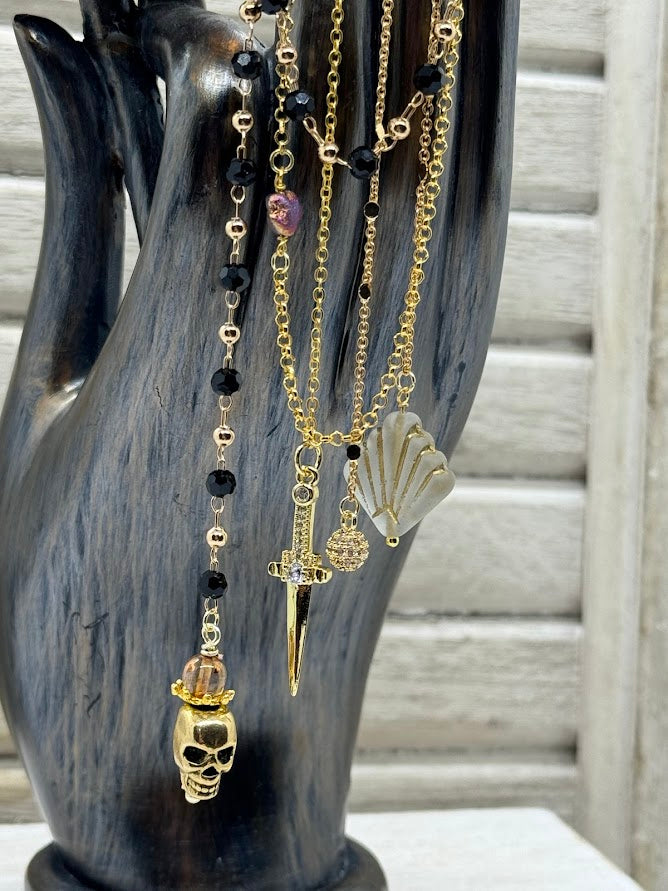 closeup of an ear hanger with a cz dagger charm, a skull charm, and a baroque style fan shaped bead.