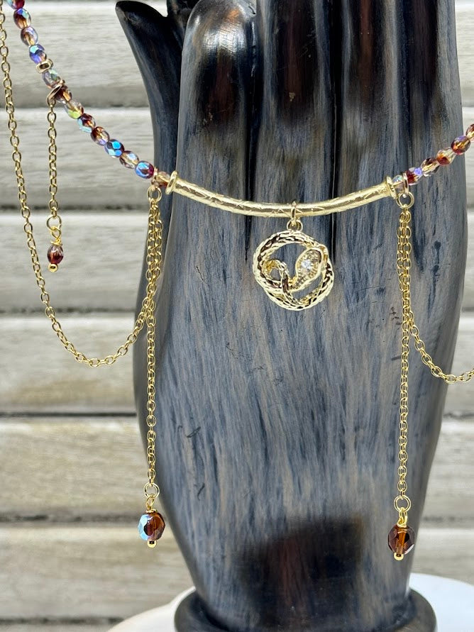 a closeup picture of a coiled snake charm. next to the charm are gold chains hanging off the red choker.