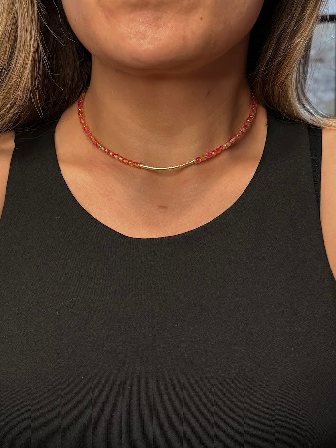 a photo of a woman in a black tank top wearing a pink and yellow choker.