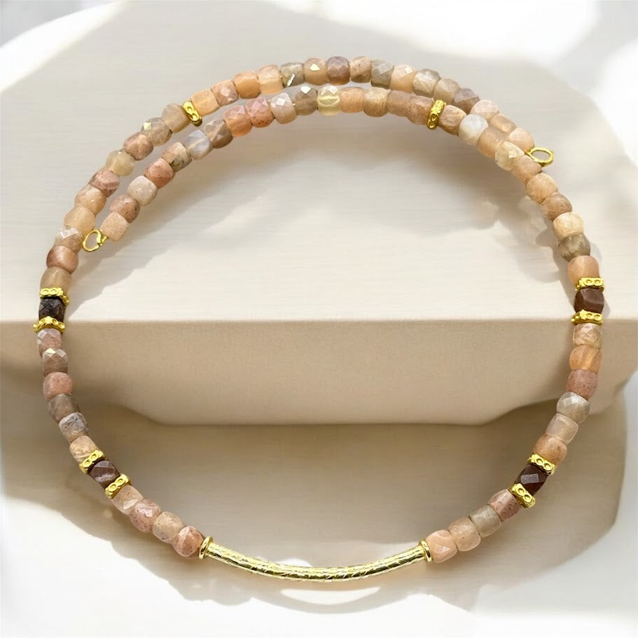 A photo of a choker made up of sunstone beads with gold accents. There is a gold bar as the center pendant for the choker